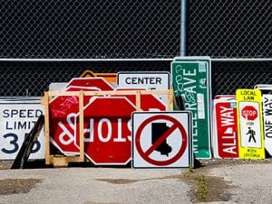 A plethora of colorful stop, speed limit, and other street signs lay against a chicken-wire fence