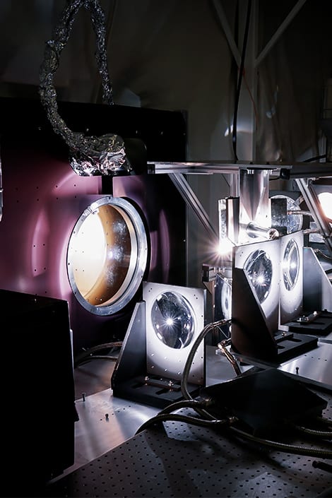 A series of optical lenses are gathered around a purple light source in a lab