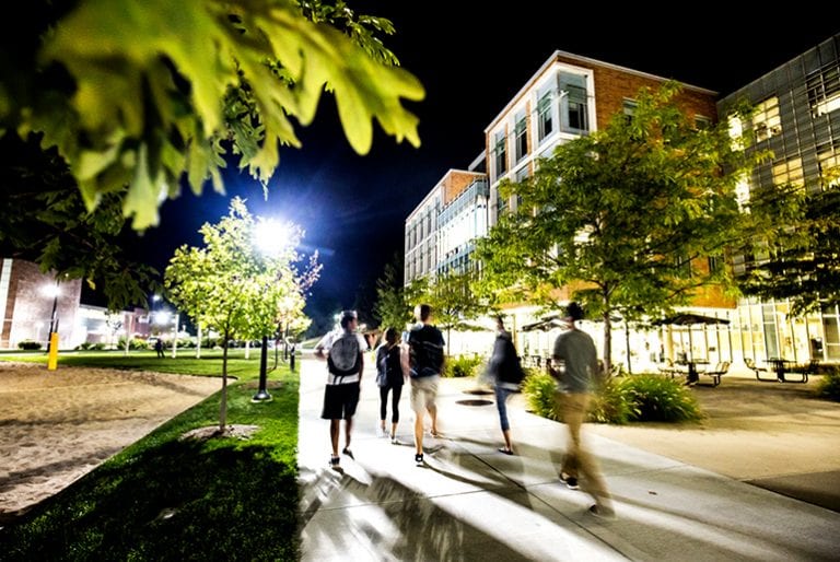Students walk in a blur through the tree-filled North Campus Grove against a midnight blue sky