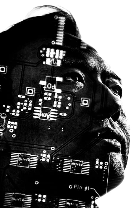 A stylized black and white image of a man looking up with a circuitboard outline layered over his face