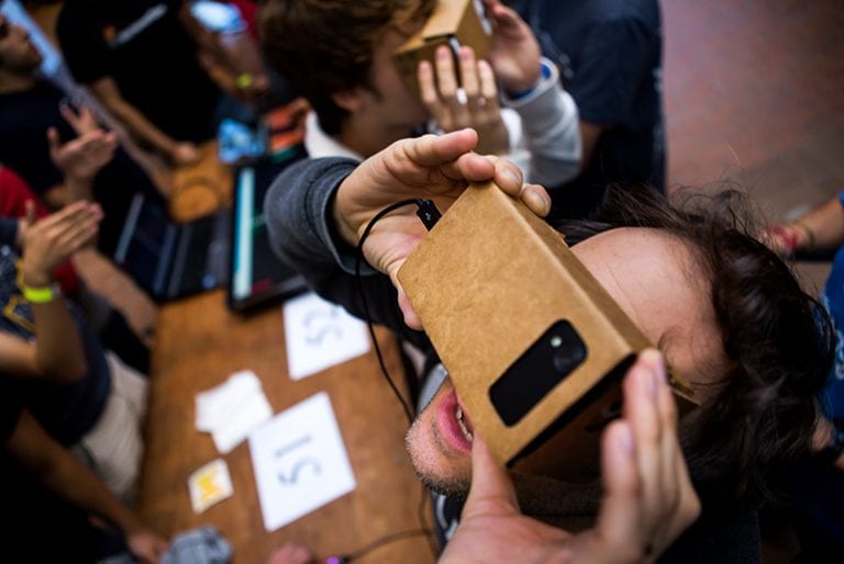 A student looks up wile experiencing virtual reality through a smartphone placed in a small cardboard box over his eyes
