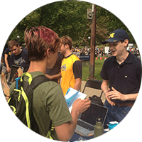 A student with colorful hair discusses ASME with a student wearing a Michigan hat at Northfest