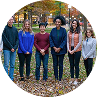 Students gather and smile for a photo in the fall with leaves all over the ground.