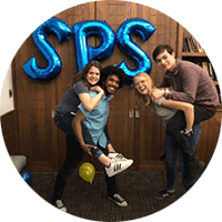 two sets of students giving each other piggy back rides laugh in front of blue balloons spelling "SPS"