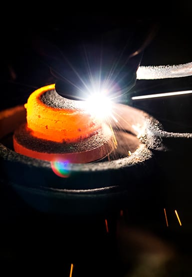 A hammer strikes a red-hot metal that glints with light