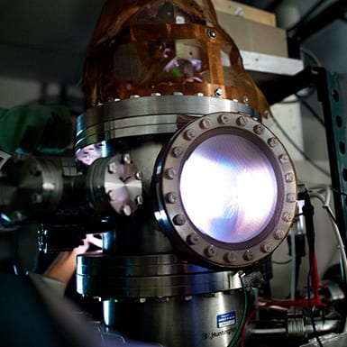 An experiment for developing better interplanetary transport glows blue and purple in a metal thruster discharge chamber