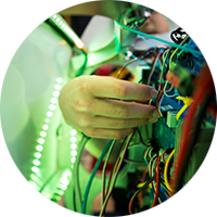 A hand adjusts the brightly colored wires with a green light shining in the background