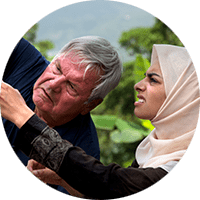 A woman in a hijab squints at a measuring tape held against a pole by an older man