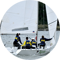 4 members of the UM Sailing team wearing block M lifejackets adjust the sails on a small white sailboat
