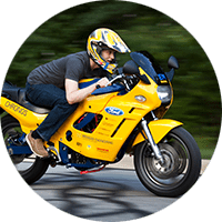A student in a full-face motorcycle helmet sits nearly horizontally as he rides the maize electric motorcycle named “Chronos”