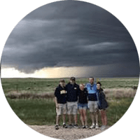 5 students gather in heavy winds to pose as a tornado forms in the background